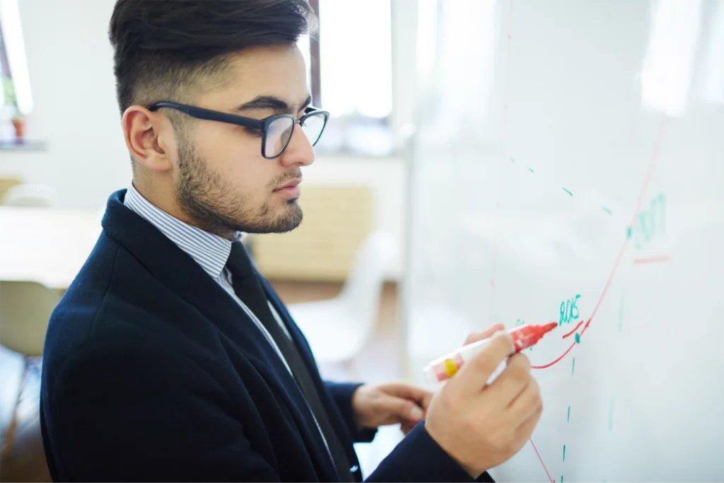 A business executive wearing glasses planning his teams CPD schedule on a whiteboard